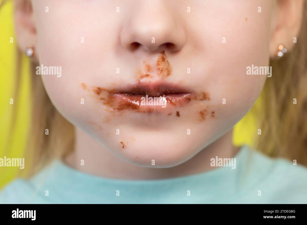 Little girl's mouth dirty with chocolate on a yellow background. Concept of children with a sweet tooth. Stock Photo