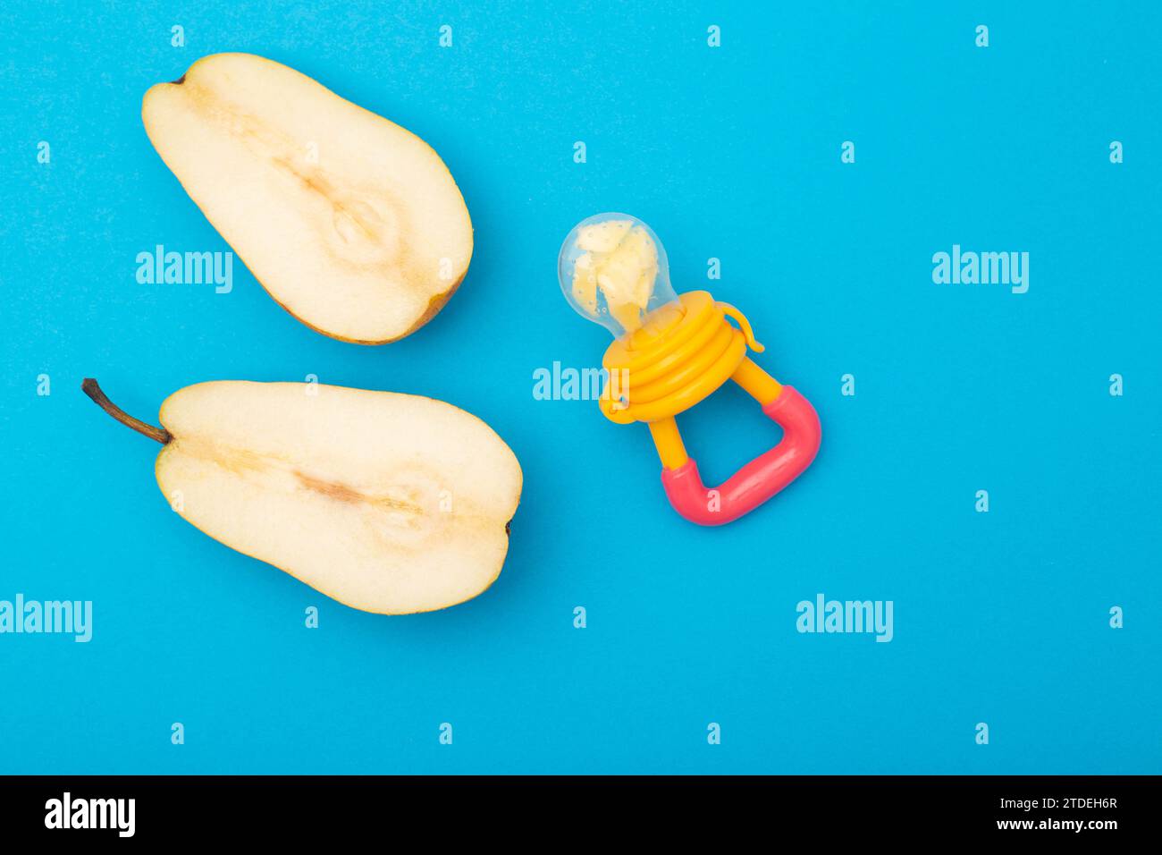 A pear cut in half on a blue background and a baby nibbler for feeding