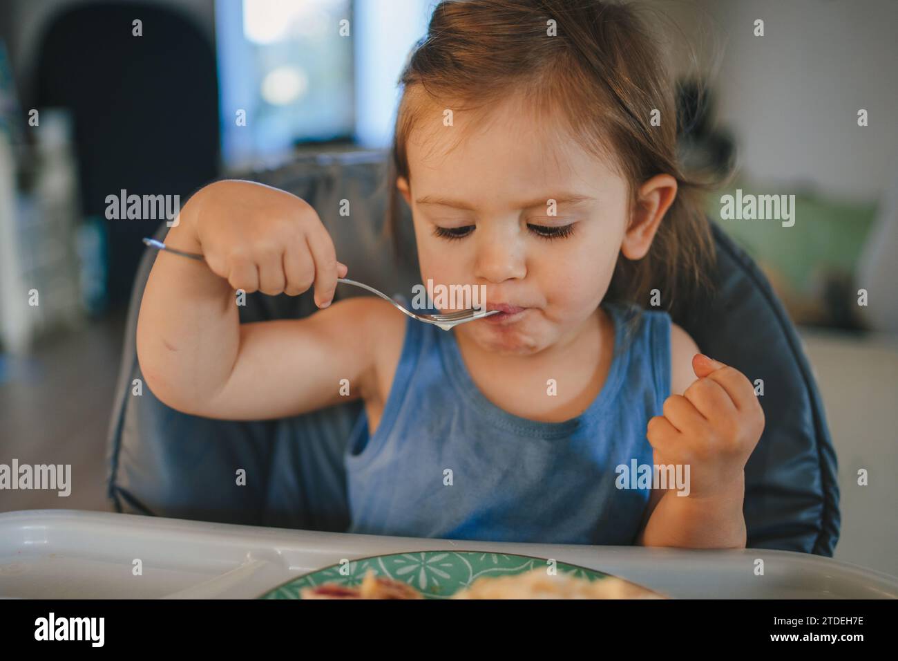 One year old hungry girl sitting at table in highchair and eating ...