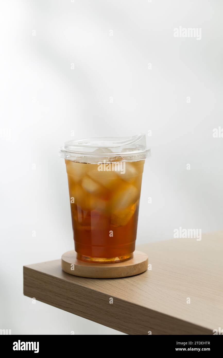 Iced tea in a clear plastic glass on a wooden table with a white background. Stock Photo