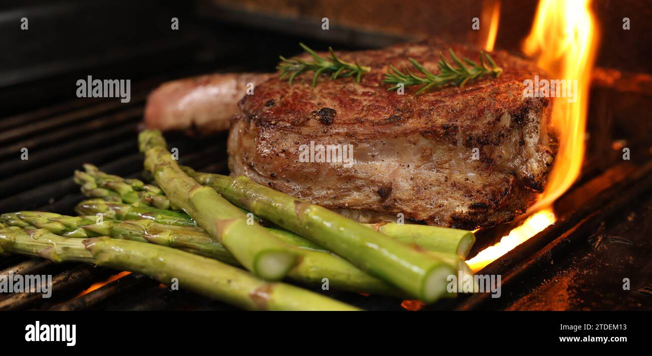 Cooking a rib-eye steak on a grill, griller or bbq. A large rib eye with bone-in sizzling away of a barbecue with flame or flare-up. Beef meat concept Stock Photo