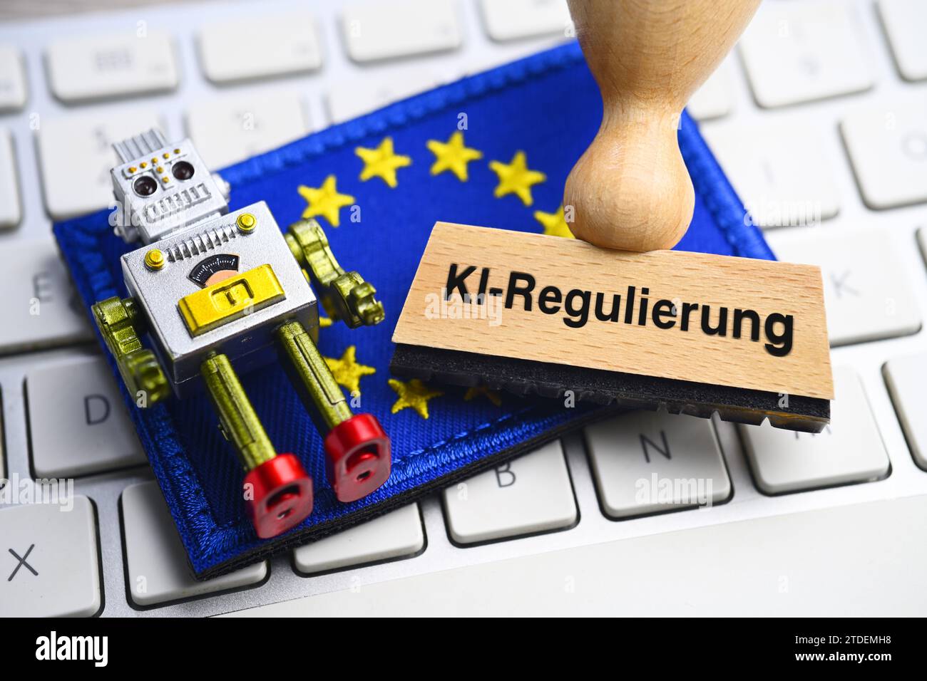 Miniature Robots And Stamps Marked AI-regulation On A Computer Keyboard In Front Of A European Flag, Photomontage Stock Photo