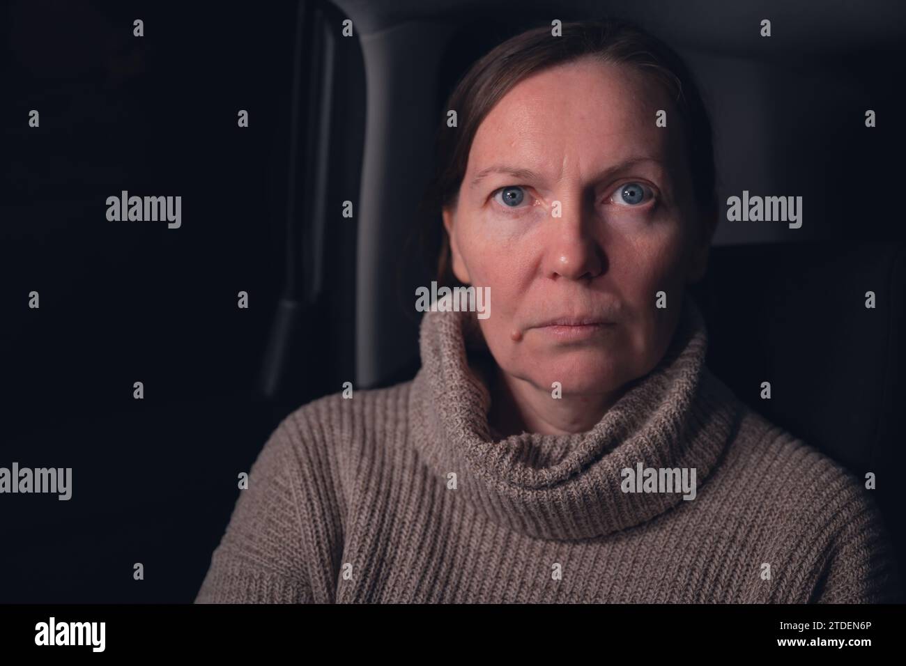 Low key portrait of serious caucasian mid adult woman at car back seat at night, looking at camera, selective focus Stock Photo