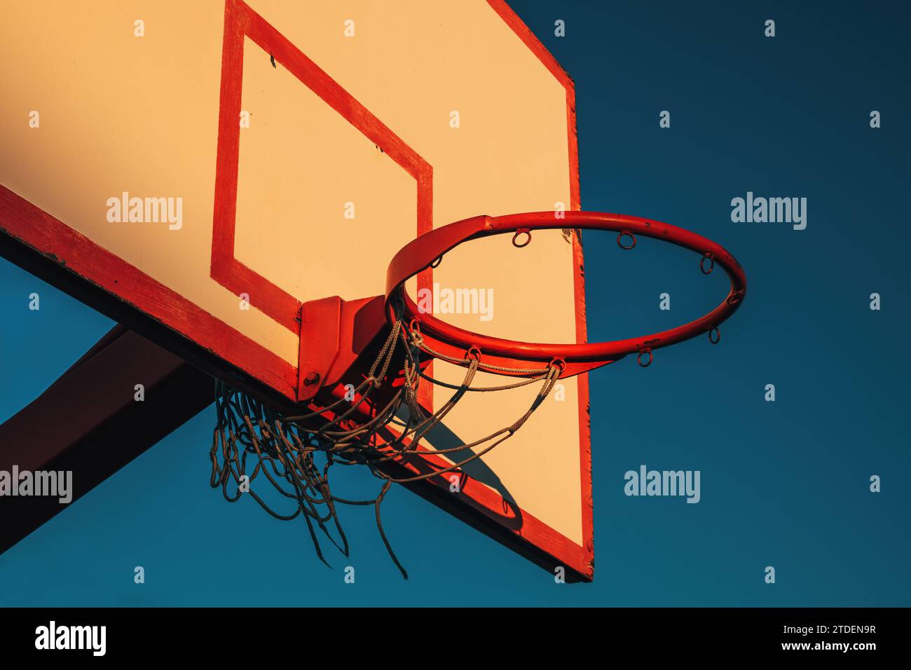 Outdoor basketball board with hoops and torn net in sunset with blue sky in background Stock Photo