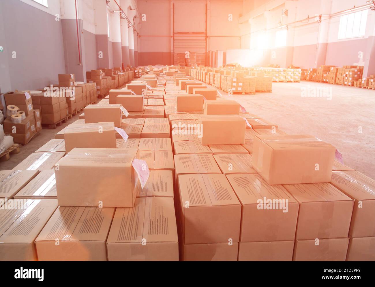 Many cardboard boxes with packaged products in a warehouse against a sunset background. Concept