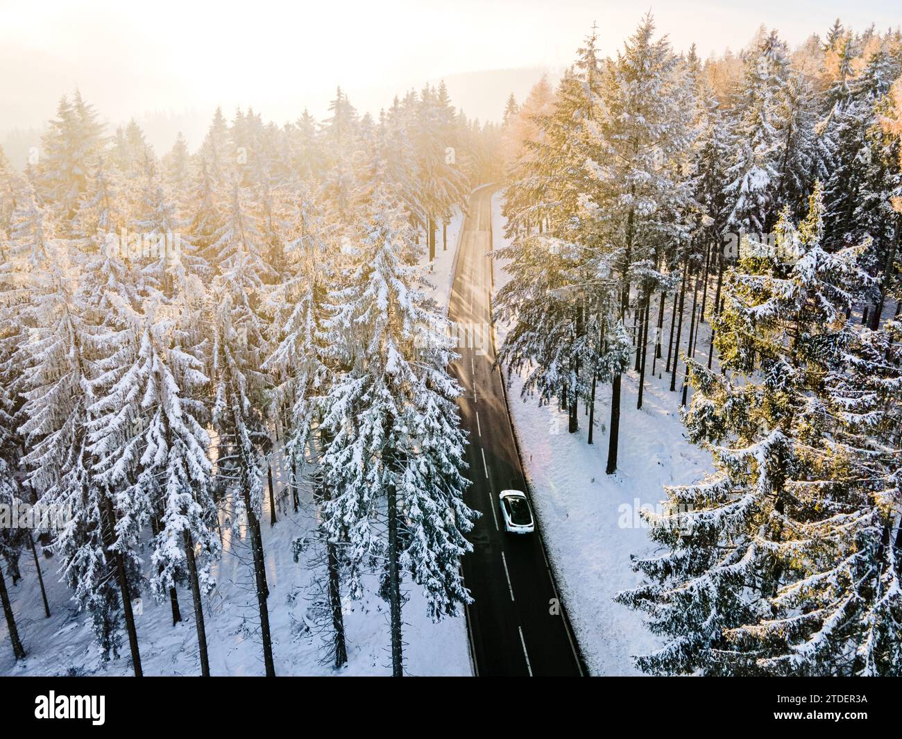 An aerial photograph capturing a mesmerizing winter scene in Feldberg, Hessen. The composition features a solitary vehicle traveling down a snow-lined Stock Photo