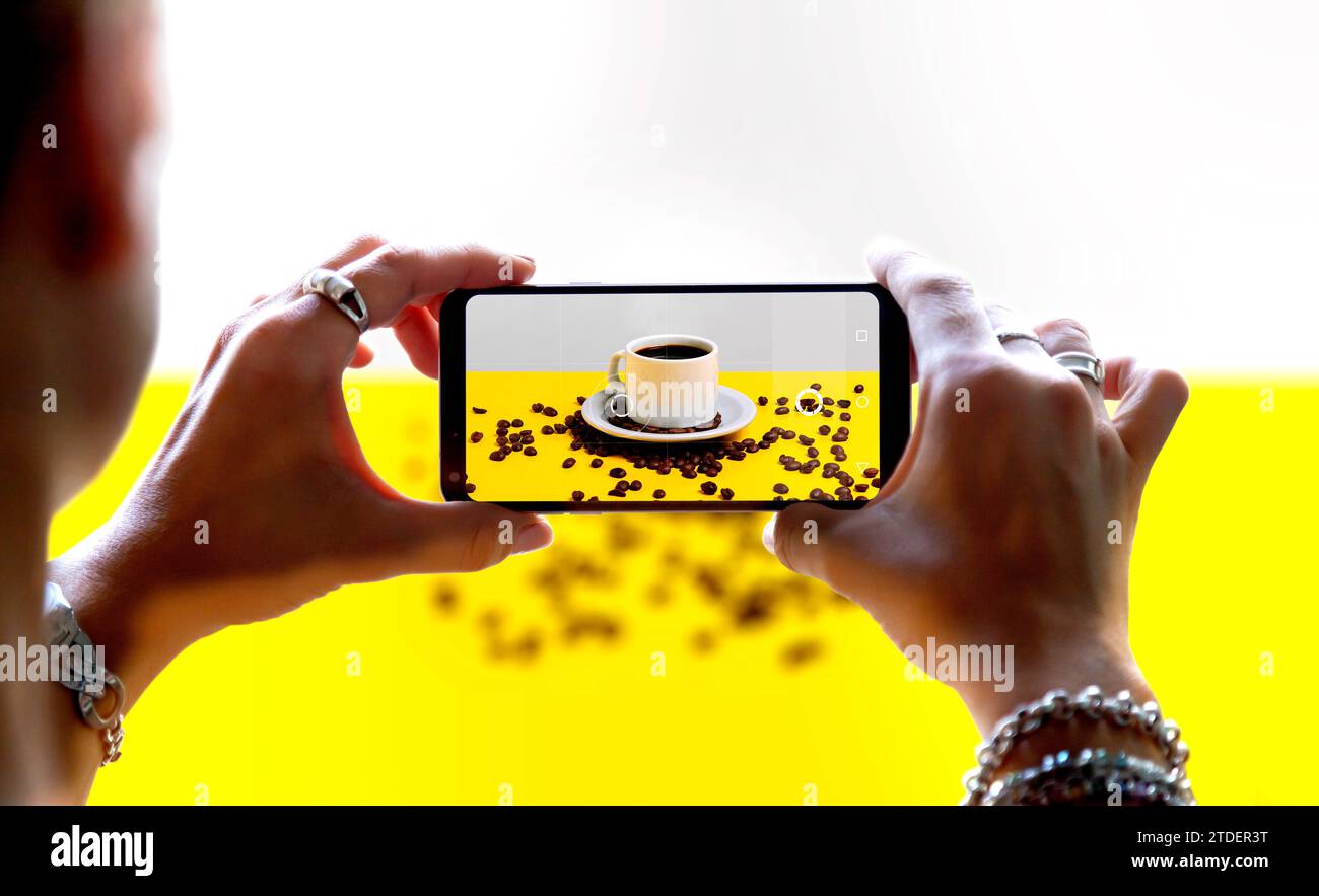 Woman using a smartphone camera to take a photo of a coffee. While shooting, it is displayed on the mobile camera screen. Product photography concept. Stock Photo