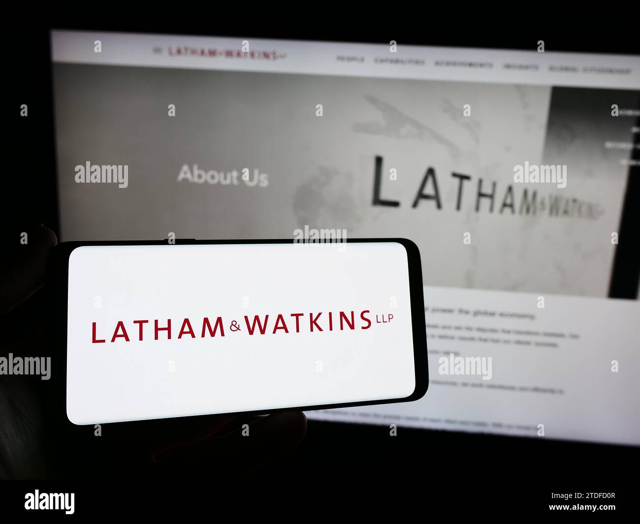 Person holding smartphone with logo of US law firm Latham and Watkins LLP (LW) in front of website. Focus on phone display. Stock Photo
