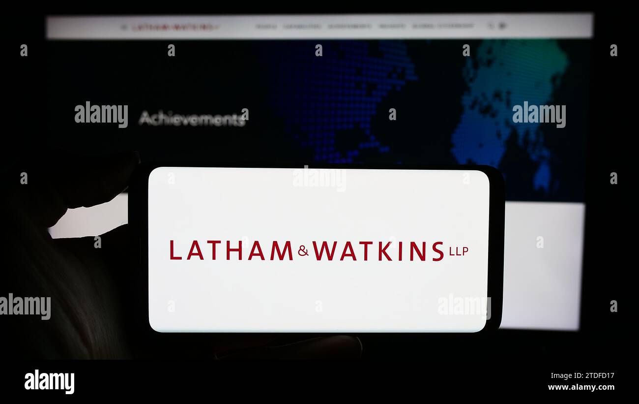 Person holding cellphone with logo of US law firm Latham and Watkins LLP (LW) in front of business webpage. Focus on phone display. Stock Photo