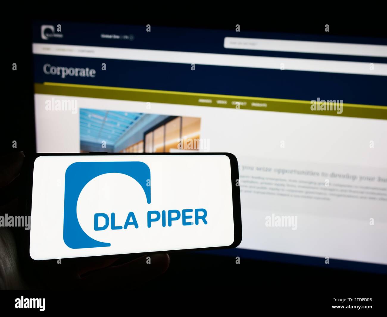 Person holding mobile phone with logo of law firm DLA Piper in front of business web page. Focus on phone display. Stock Photo