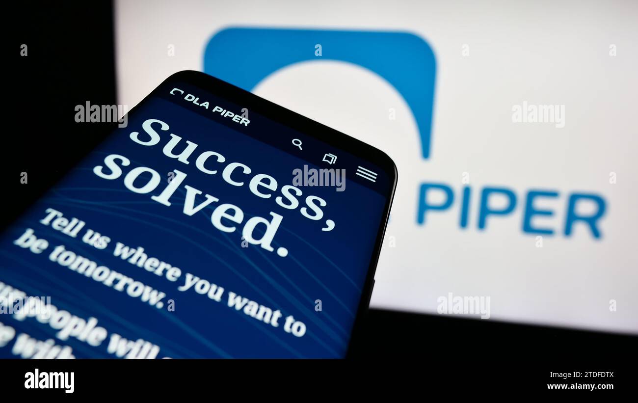 Mobile phone with website of law firm DLA Piper in front of business logo. Focus on top-left of phone display. Stock Photo