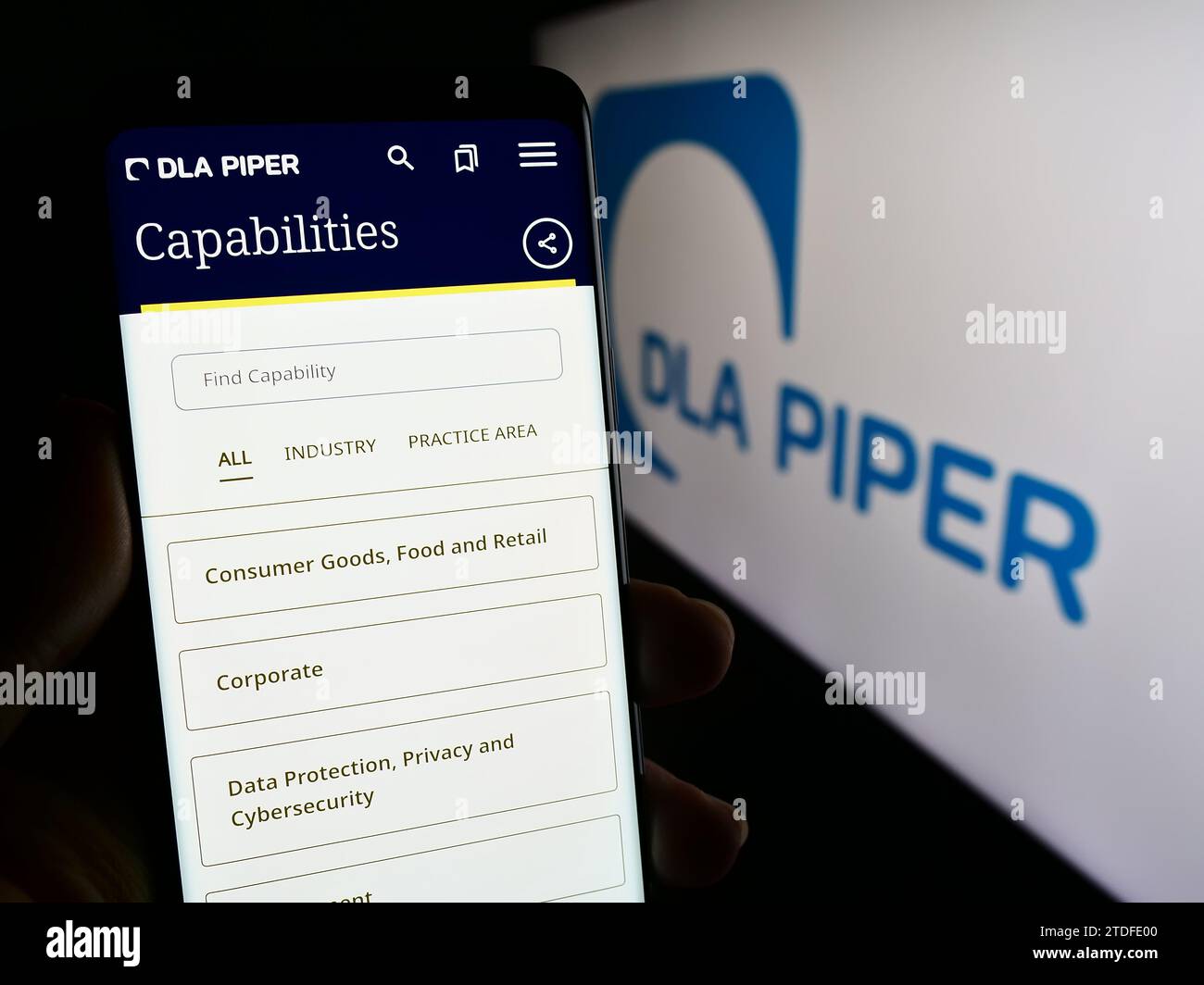 Person holding cellphone with web page of law firm DLA Piper in front of business logo. Focus on center of phone display. Stock Photo