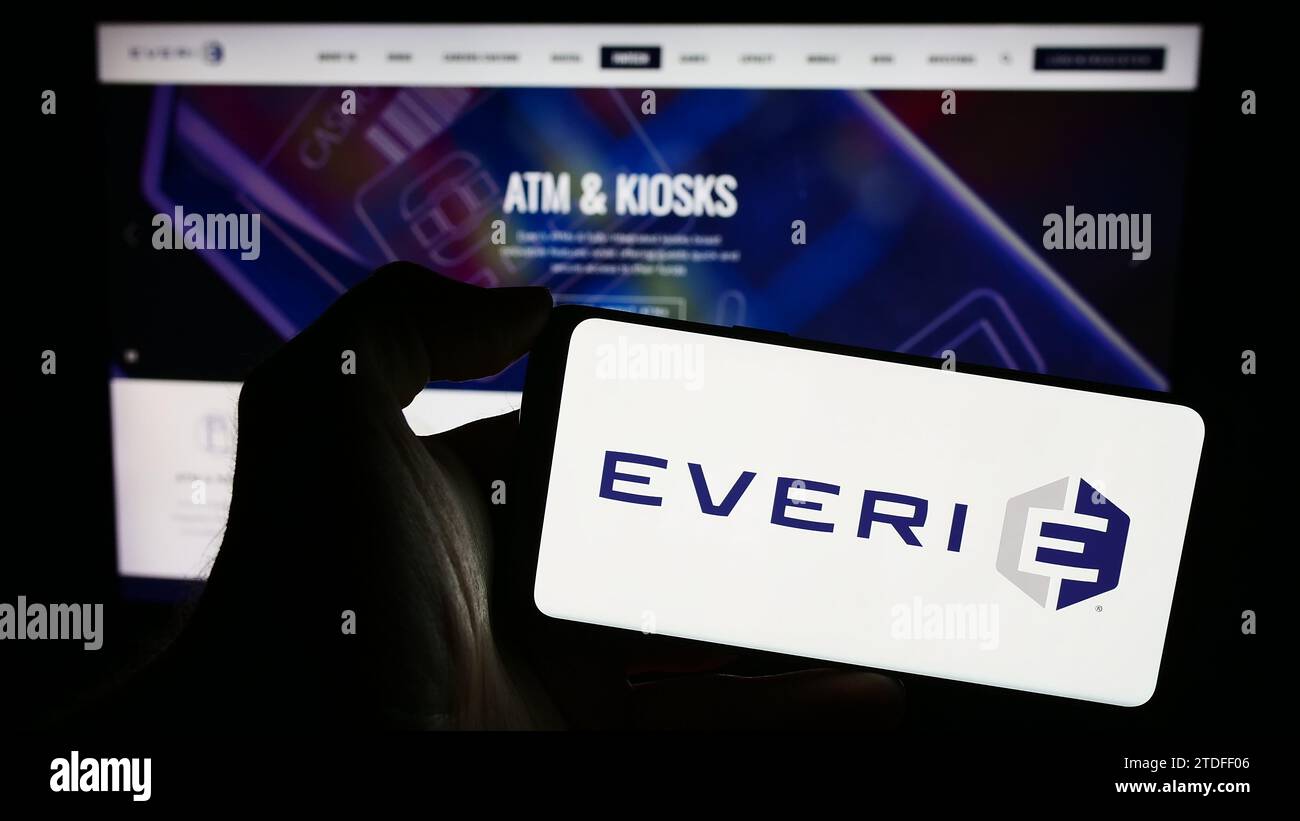 Person holding smartphone with logo of US slot machine company Everi Holdings Inc. in front of website. Focus on phone display. Stock Photo