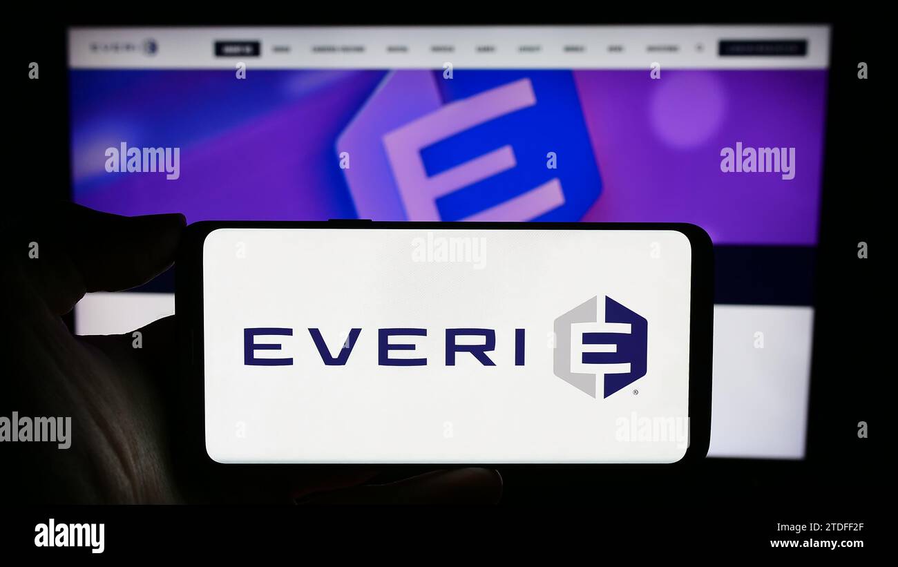 Person holding cellphone with logo of US slot machine company Everi Holdings Inc. in front of business webpage. Focus on phone display. Stock Photo