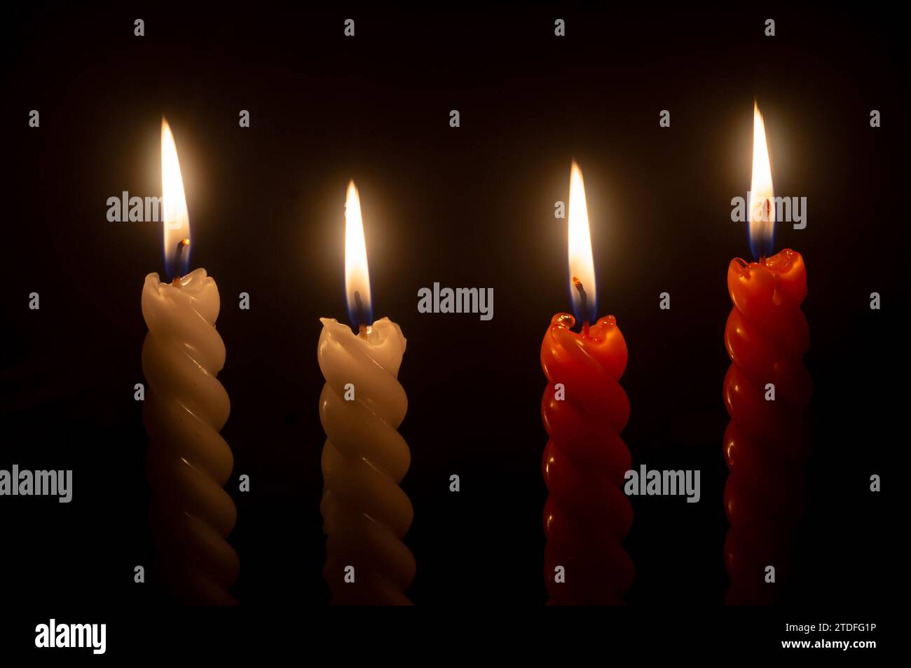 burning candle flame or light is glowing on four spiral candles on black or dark background on table in church for Christmas, funeral or memorial Stock Photo