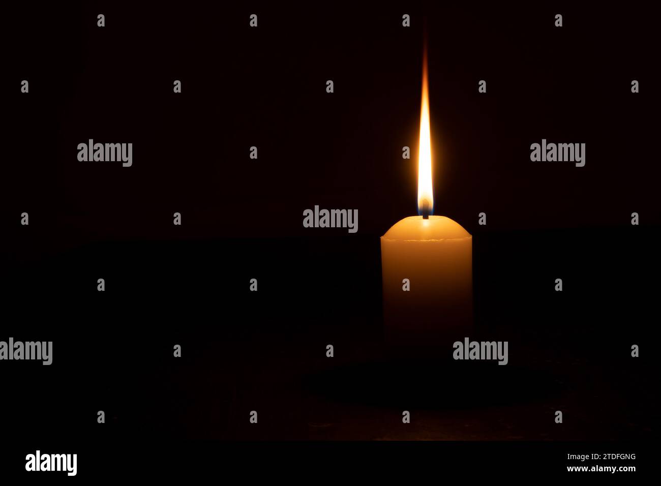 A single burning candle flame or light is glowing on a yellow candle