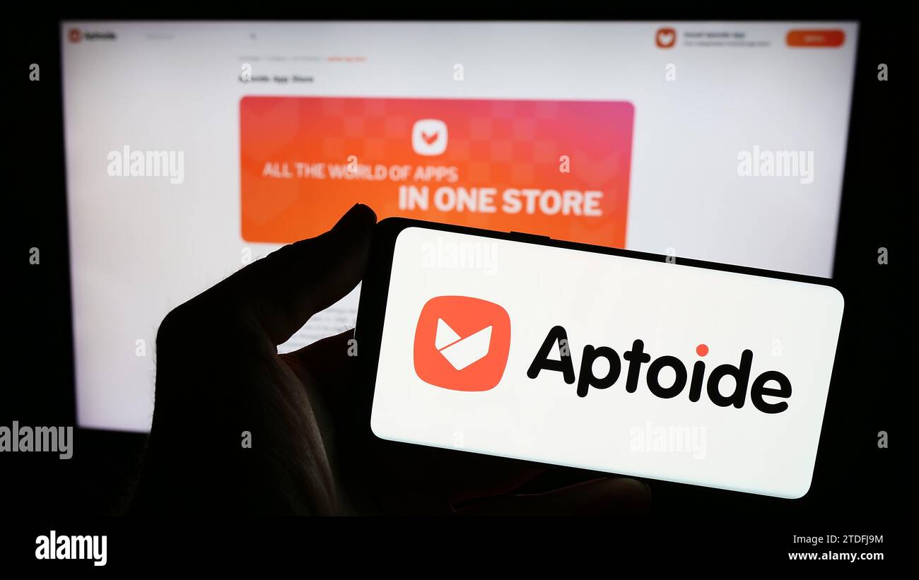 Person holding smartphone with logo of Portuguese app marketplace company Aptoide S.A. in front of website. Focus on phone display. Stock Photo
