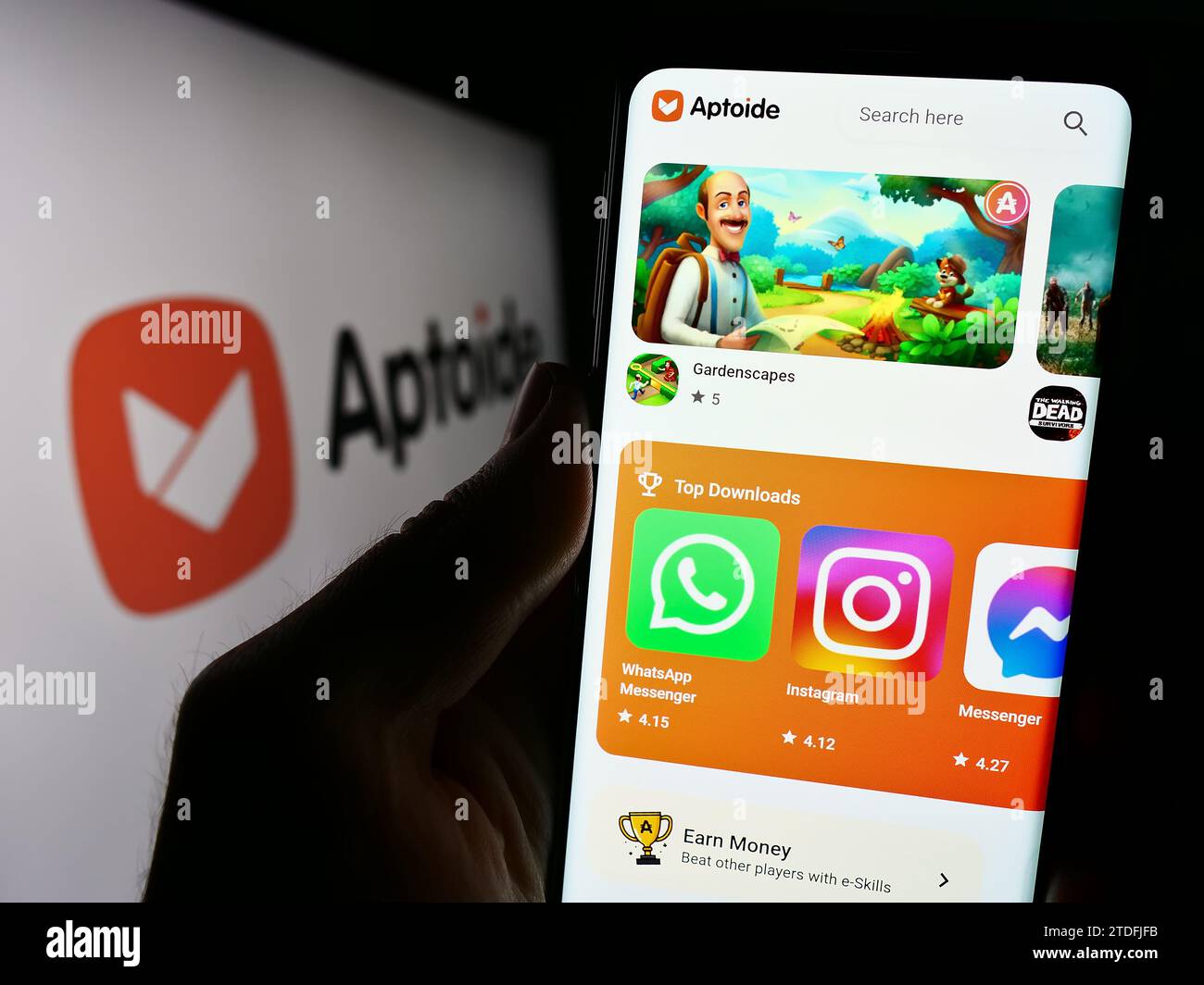 Person holding cellphone with webpage of Portuguese app marketplace company Aptoide S.A. in front of logo. Focus on center of phone display. Stock Photo