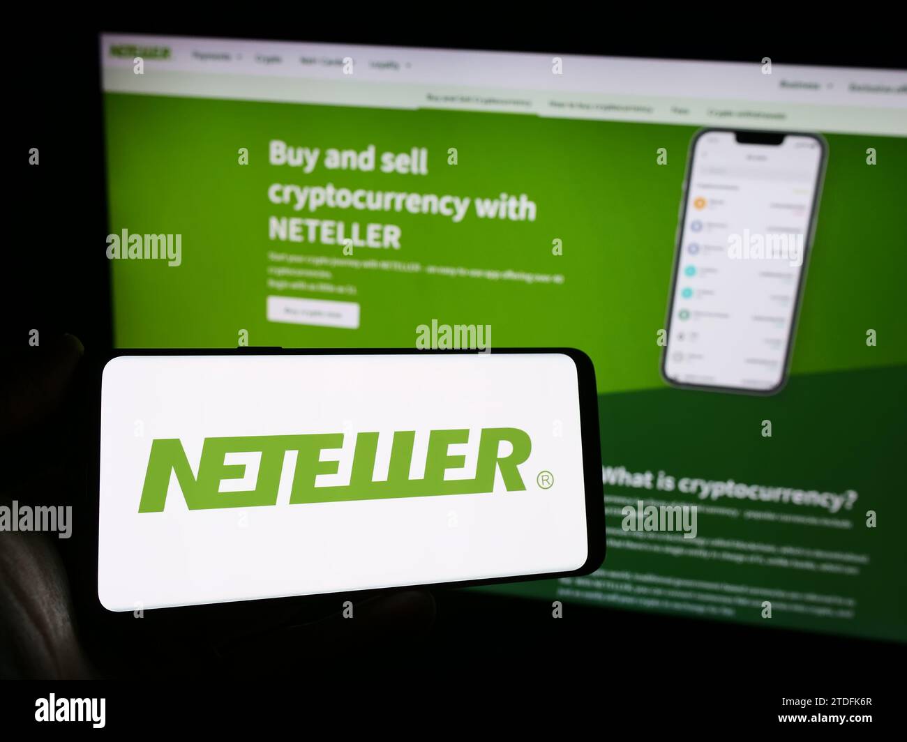 Person holding mobile phone with logo of global payments platform company Neteller in front of business web page. Focus on phone display. Stock Photo