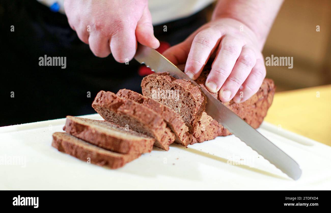 24.08.2011, Deutschland, auf dem Foto zwei Hände welche ein Kastenbrot mit einem scharfen Brotmesser auf einem Tablett schneiden *** 24 08 2011, Germany, on the photo two hands cutting a loaf of bread with a sharp bread knife on a tray Stock Photo