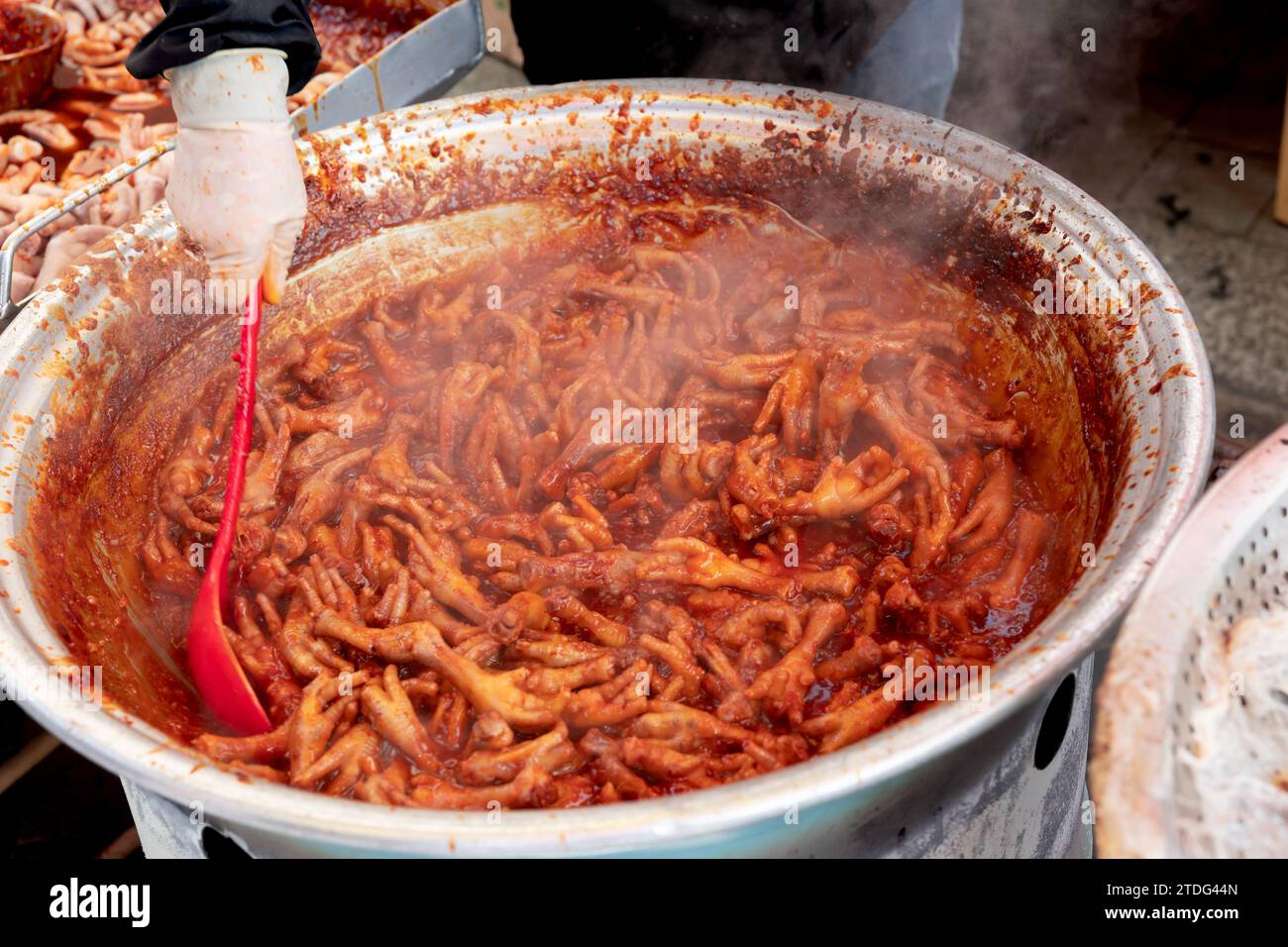 Stir-fried chicken feet for sale at a traditional market in Korea and a merchant's hand cooking with a ladle Stock Photo