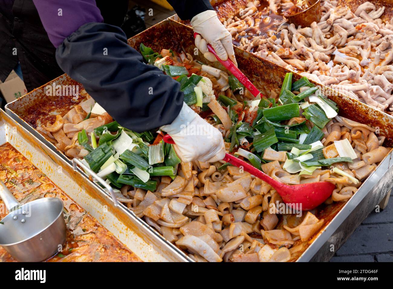 Stir-fried pork rinds for sale at a traditional market in Korea and a vendor's hand cooking with a ladle Stock Photo