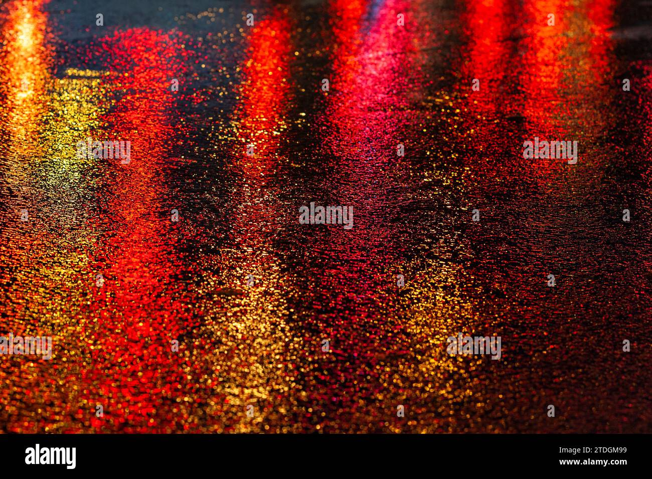Abstract, wet asphalt road colorfully illuminated at night by red car ...