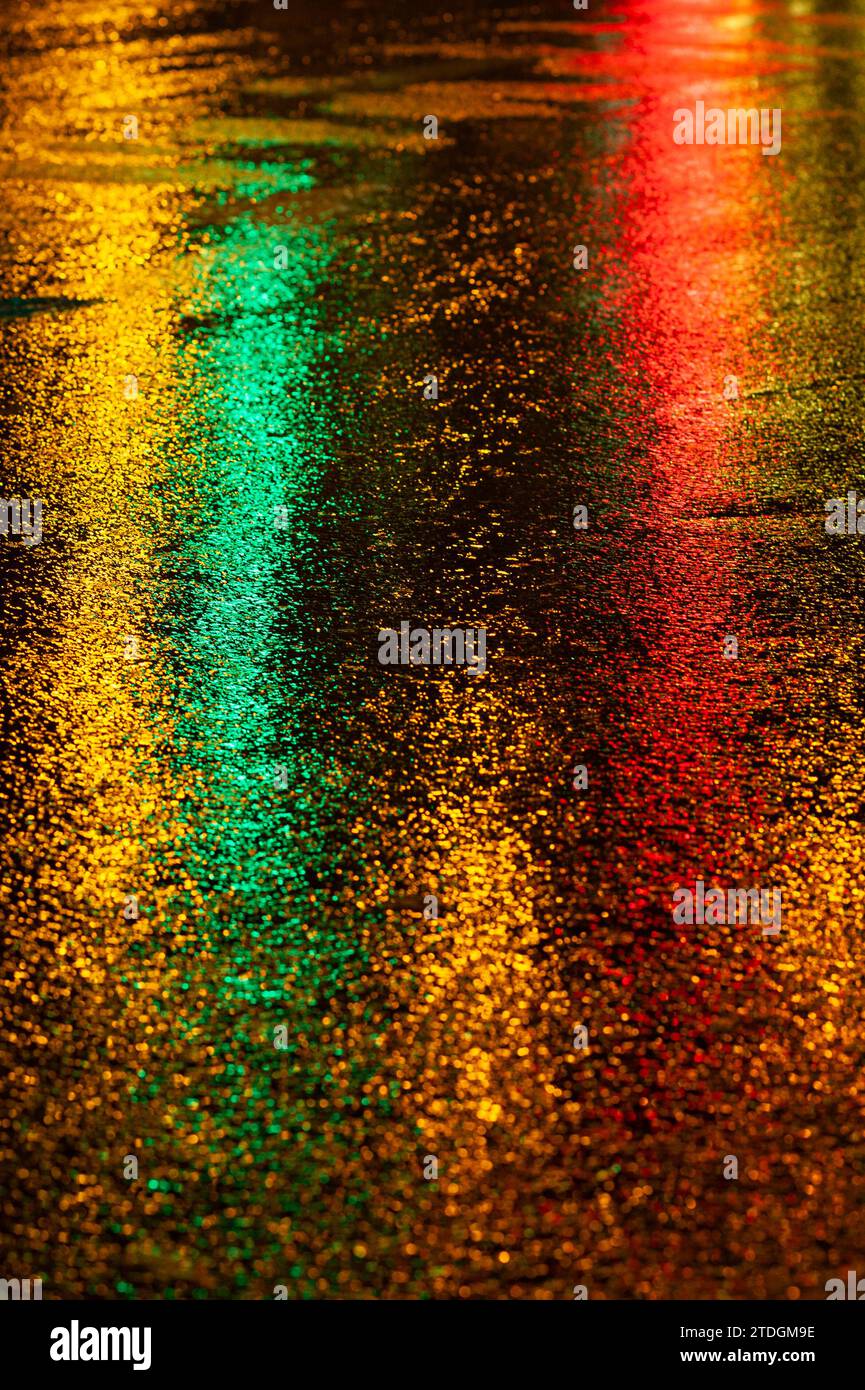 Abstract, wet asphalt road colorfully illuminated at night by red car ...