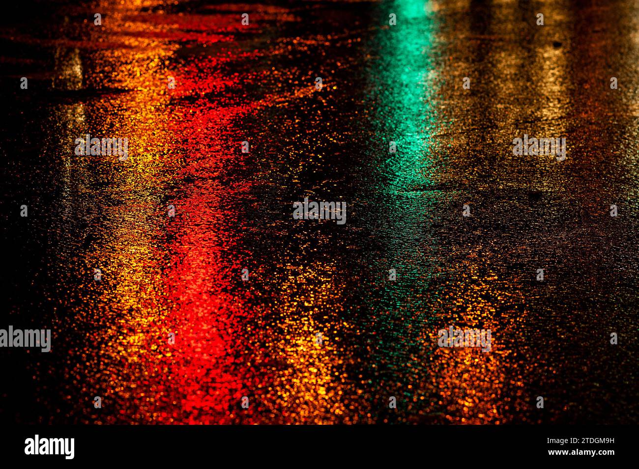 Abstract, wet asphalt road colorfully illuminated at night by red car ...