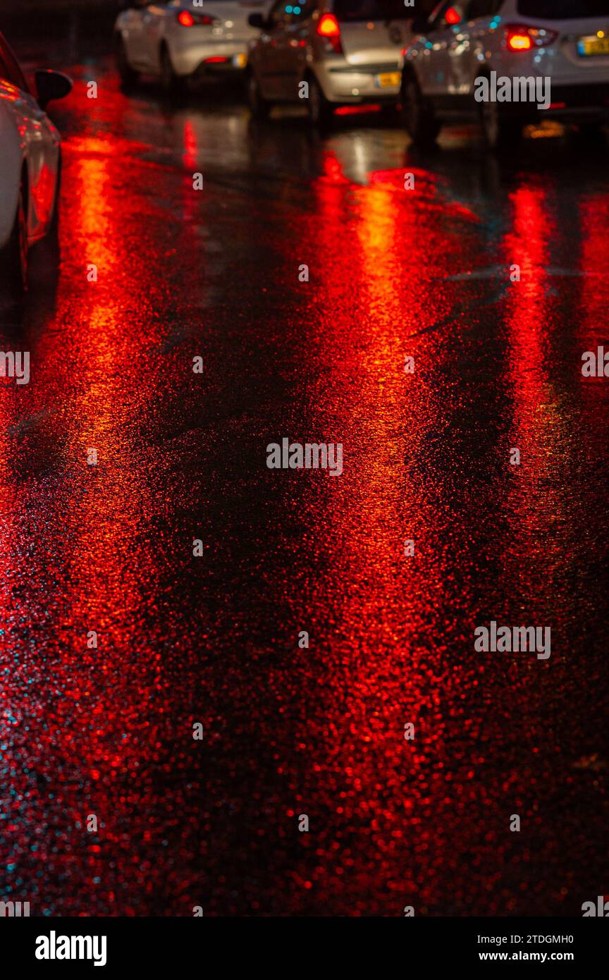 Abstract, wet asphalt road colorfully illuminated at night by red car ...