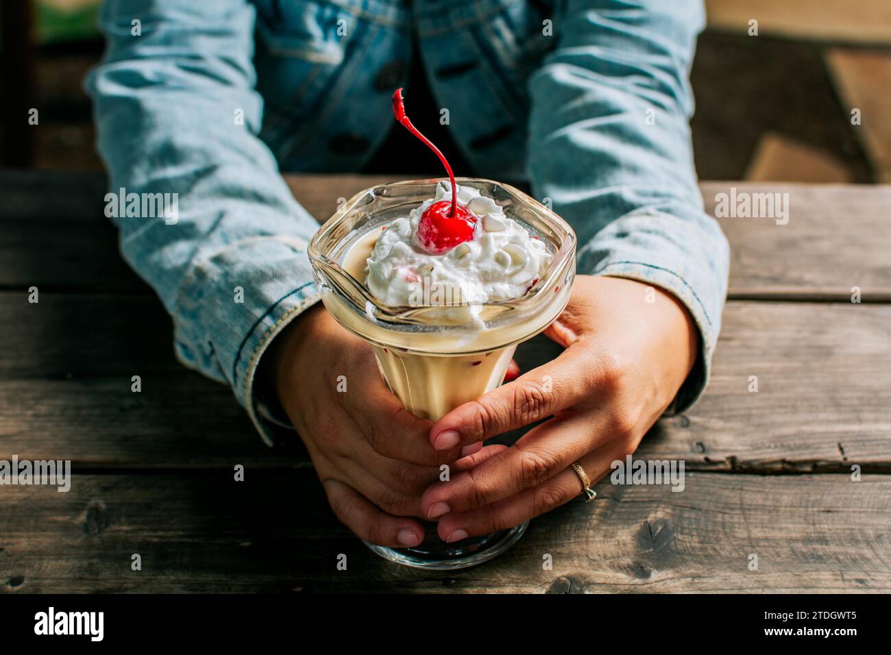 Female hand holding cherry milkshake on wooden table. Person holding cherry smoothie over wooden table Stock Photo