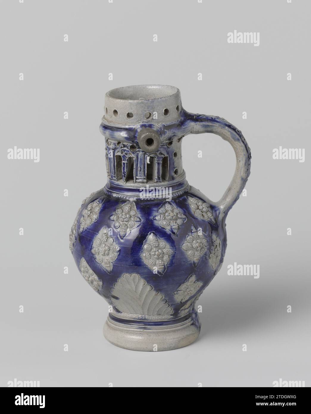 Jug with foliate ornaments and medallions, anonymous, c. 1650 - c. 1724 Can (Fopkan) of stoneware on high foot with a spherical belly and openwork neck with just below the edge a short spout. The C-shaped ear is attached to the neck and shoulder. At the bottom of the jug there is a hole on the inside, so that the liquid can flow out through the spout through a tube in the wall, ear and edge. Partly covered with cobalt blue. On the abdomen, leaf motifs and small printed and imposed, diamond -shaped medallions with flowers in relief against a blue background. On the neck in relief pillars and wi Stock Photo