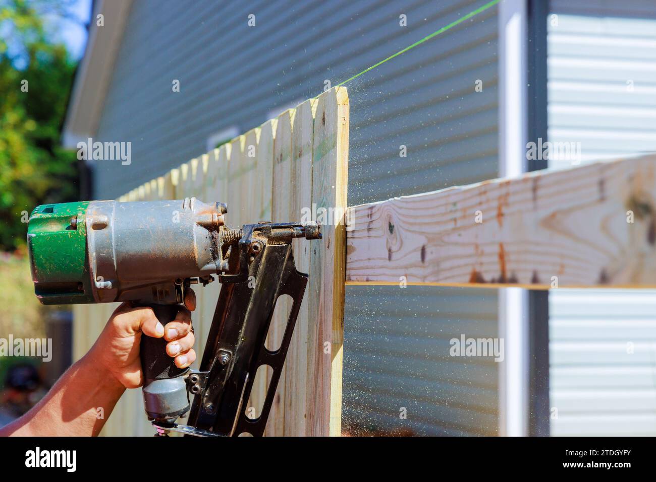 Worker uses an air nail gun to secure sections of wooden fence around