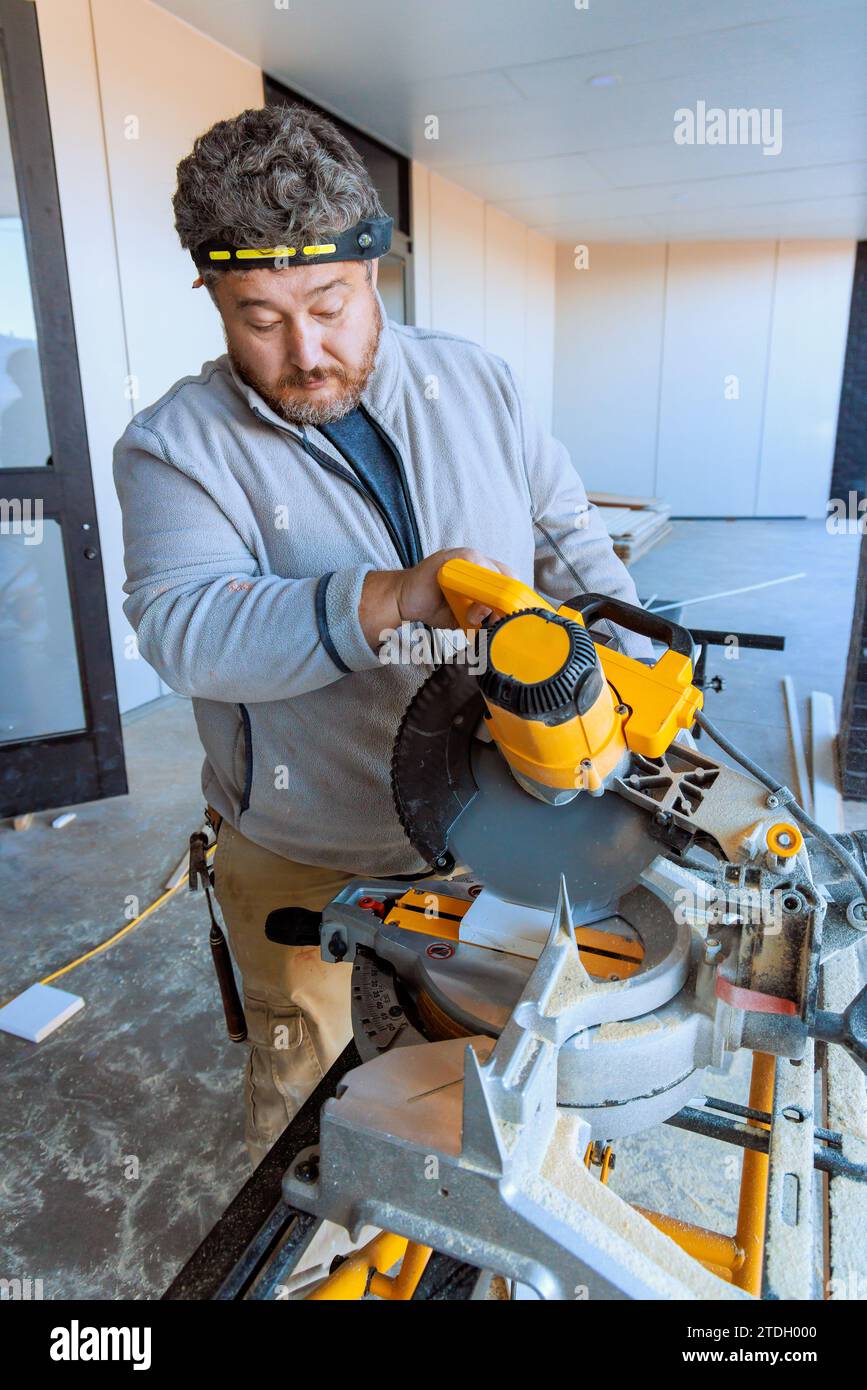 Trim worker cuts wooden moldings on chop saw Stock Photo