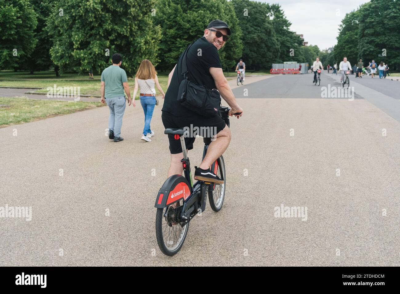 A man rides a hire / rental Santander eBike in London through a park Stock Photo