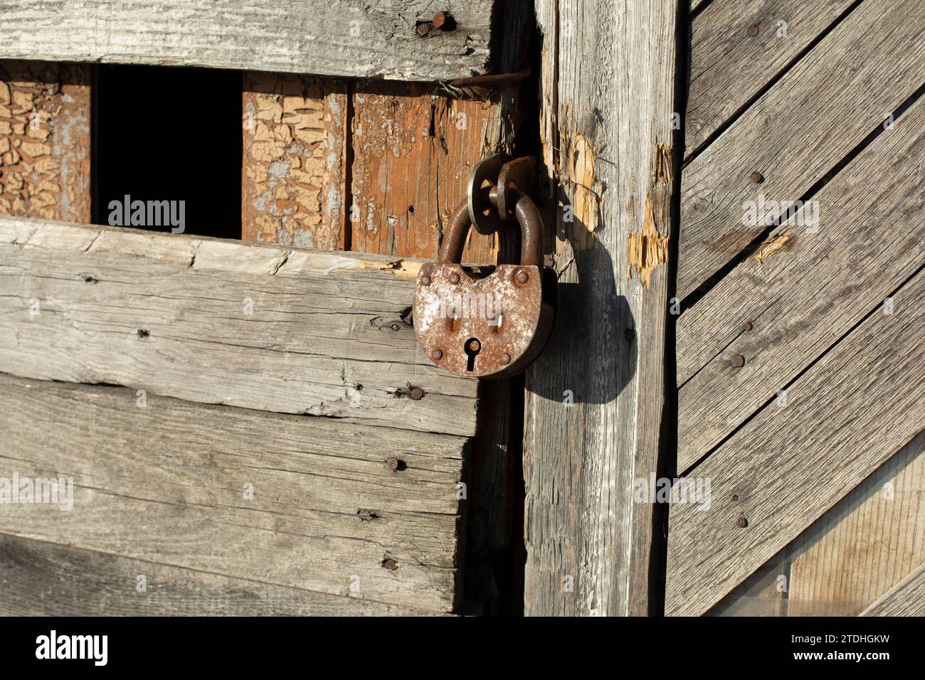 Old lock on the door. Rusty lock on the barn. The old building in detail. Made of planks. Stock Photo