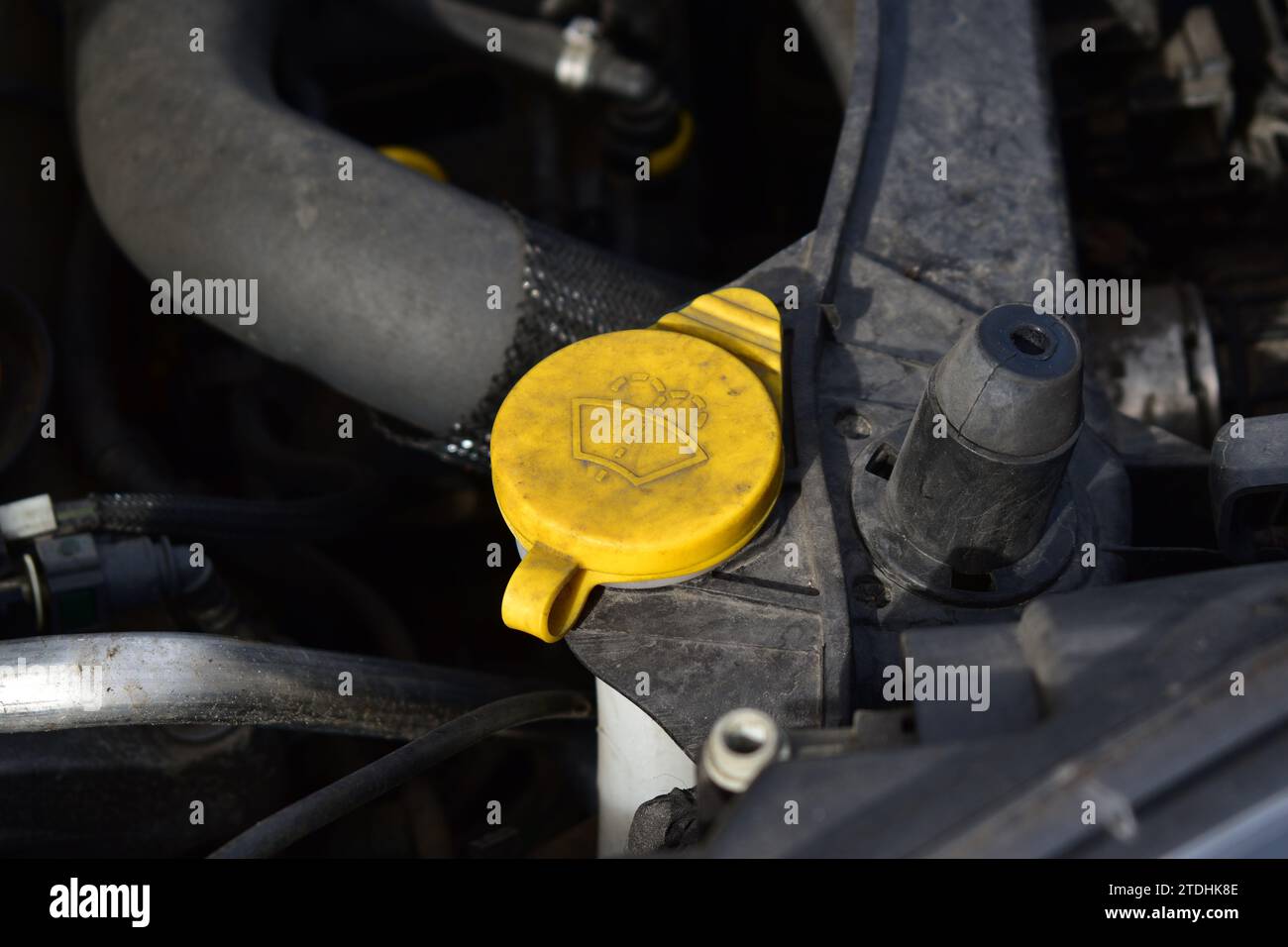 Dirty yellow cap of the windshield wiper fluid reservoir inside the engine compartment Stock Photo