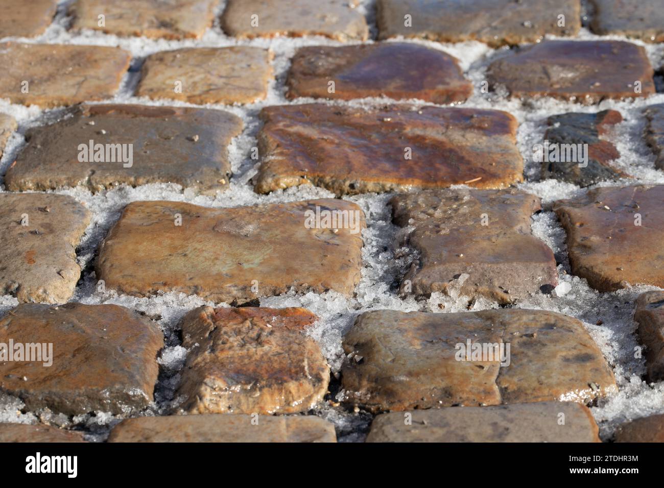 Cobblestone pavement photographed from diagonally above. There is snow in the joints. There is a danger of slipping. Stock Photo