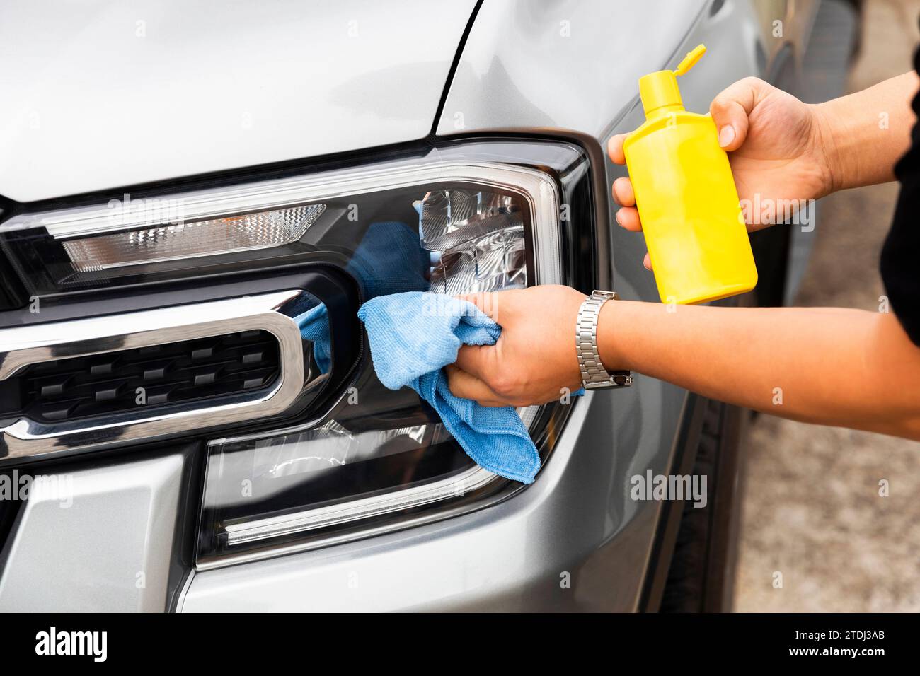 Using a cleaning spray bottle on the car's headlights ensuring a wellmaintained appearance