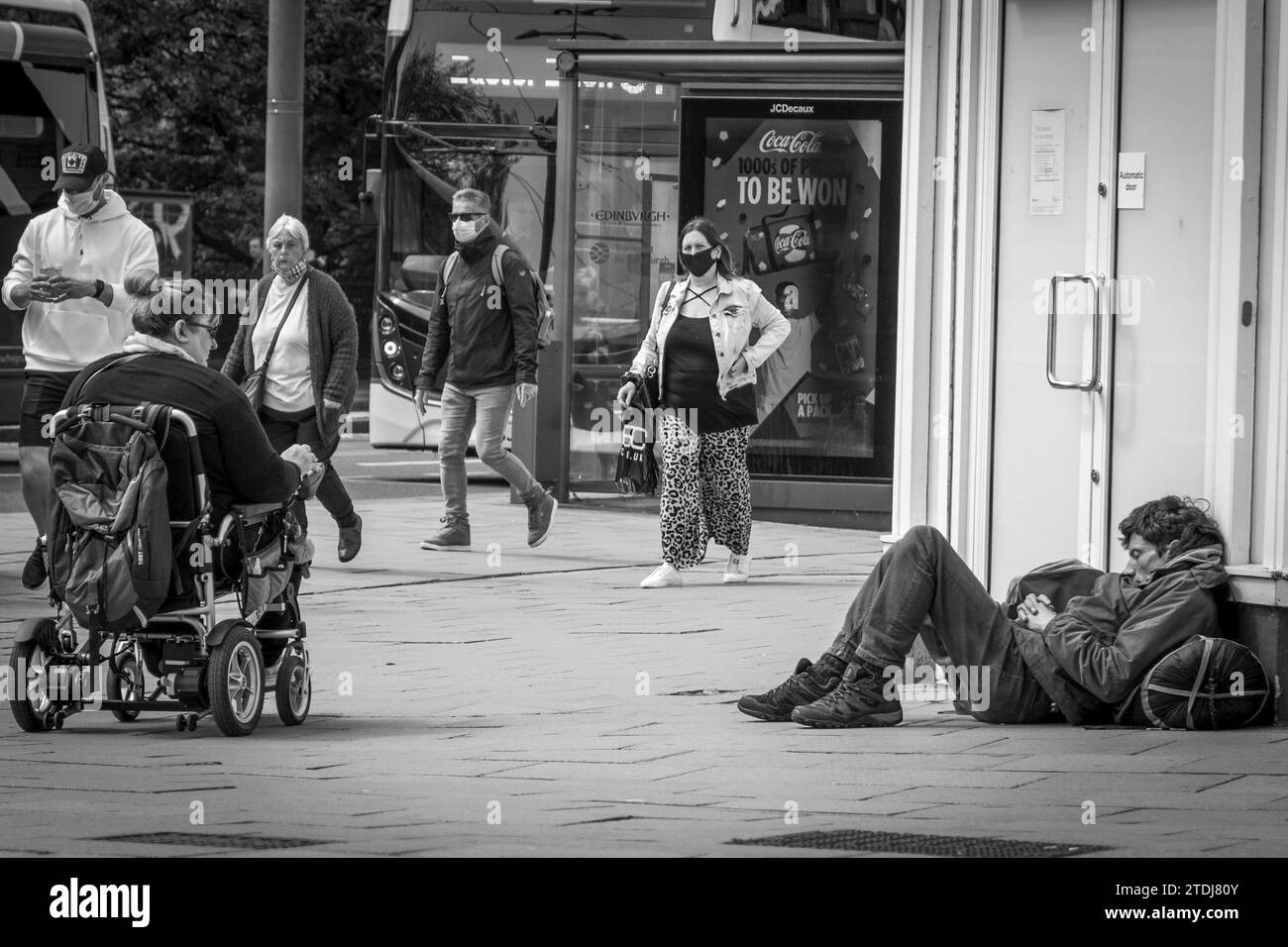 Black & White Photo - People Going Past A Homeless Person Sleeping on Castle Street, Edinburgh, Scotland UK Stock Photo