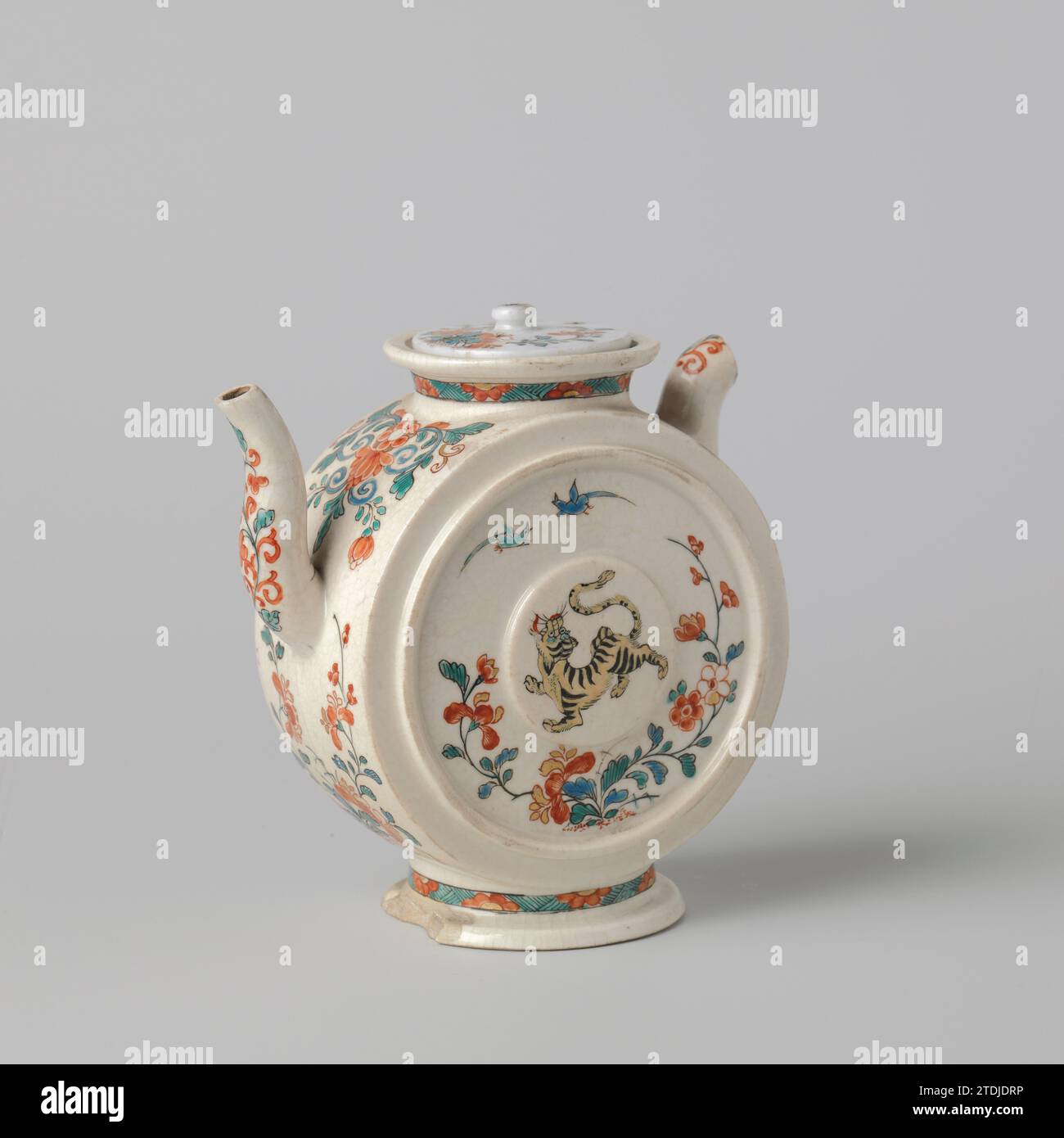 Teapot with a tiger, birds and floral scrolls, anonymous, c. 1700 - c. 1799 Teapot of Soft-Paste Porcelain (Pâte Tendre) on foot and an S-shaped spout, painted on the glaze in blue, red, green, yellow, black and gold. The belly is in the form of a cylinder standing on the side, with an elevated medallion and an elevated circle on the flat wall. On the wall a tiger, two birds and a flowering plant. The round wall, the spout and the ear with flower vines. On the neck and the foot a band with archery interrupted by half flowers. The ear has largely been broken down. Kakiemon style. Japan porcelai Stock Photo