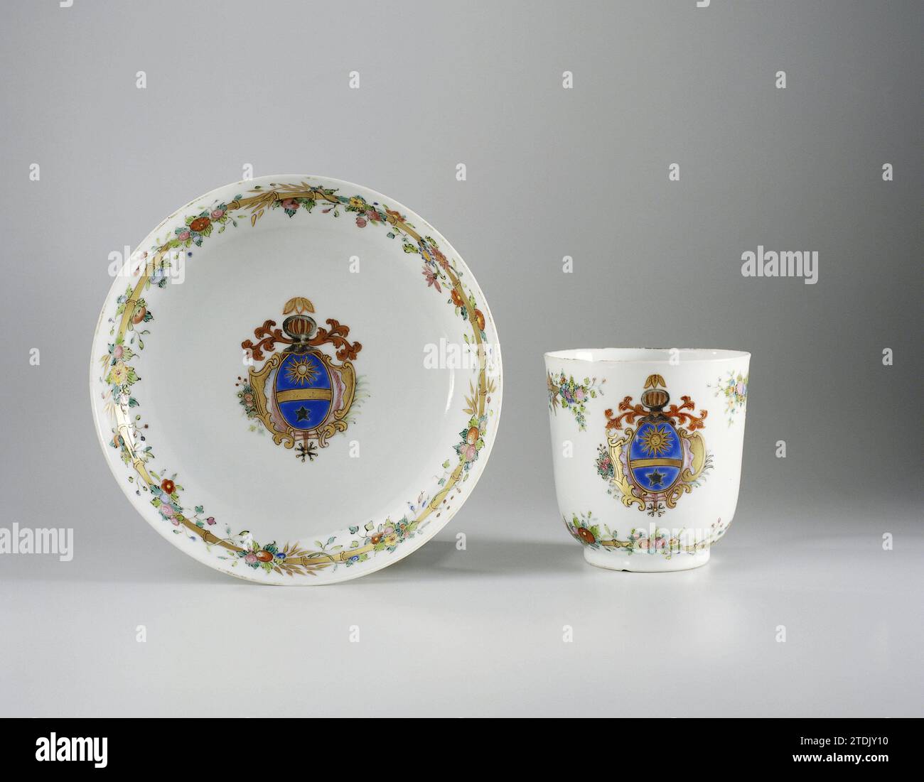 Cup with handle and saucer with a coat of arms and bamboo border with floral scrolls, anonymous, c. 1750 - c. 1774 Porcelain ear head, painted on the glaze in blue, red, pink, green, yellow, black and gold. On the flat of the dish an unidentified family crest with a sun with a face, a star and a gold beam on a blue background. The weapon is surrounded by leaf vines, a palm branch and flower branch. On the wall a bamboo band with flower vines. The head with the same decoration. A chip in the edge of the head. Weapon porcelain with email colors. China porcelain. glaze. gold (metal) painting / gi Stock Photo