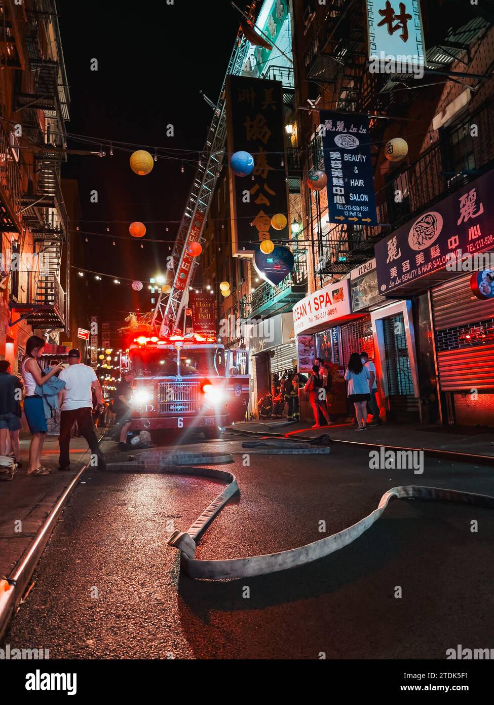 FDNY fire hoses traverse Pell St in Chinatown, New York, while a truck extends its ladder to the roof of an apartment building which was on fire Stock Photo