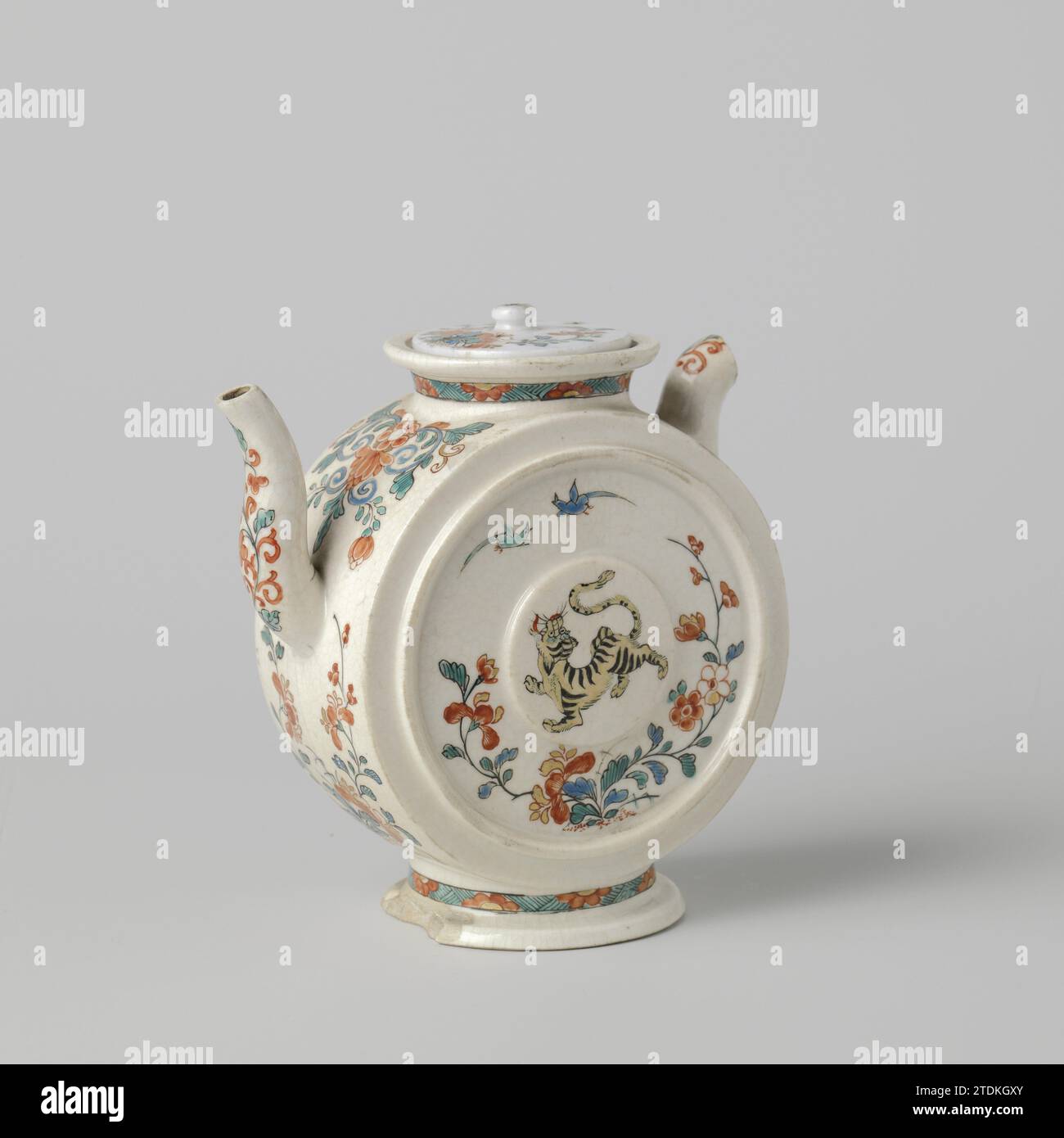 Teapot with a tiger, birds and floral scrolls, anonymous, c. 1700 - c. 1799 Teapot of Soft-Paste Porcelain (Pâte Tendre) on foot and an S-shaped spout, painted on the glaze in blue, red, green, yellow, black and gold. The belly is in the form of a cylinder standing on the side, with an elevated medallion and an elevated circle on the flat wall. On the wall a tiger, two birds and a flowering plant. The round wall, the spout and the ear with flower vines. On the neck and the foot a band with archery interrupted by half flowers. The ear has largely been broken down. Porcelain lid with flower vine Stock Photo