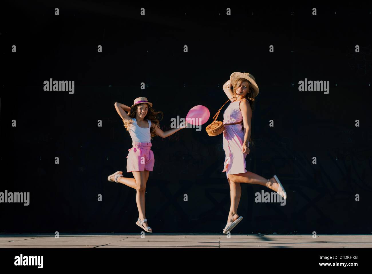 mother and daughter jumping in pink dresses with loose long hair on a ...