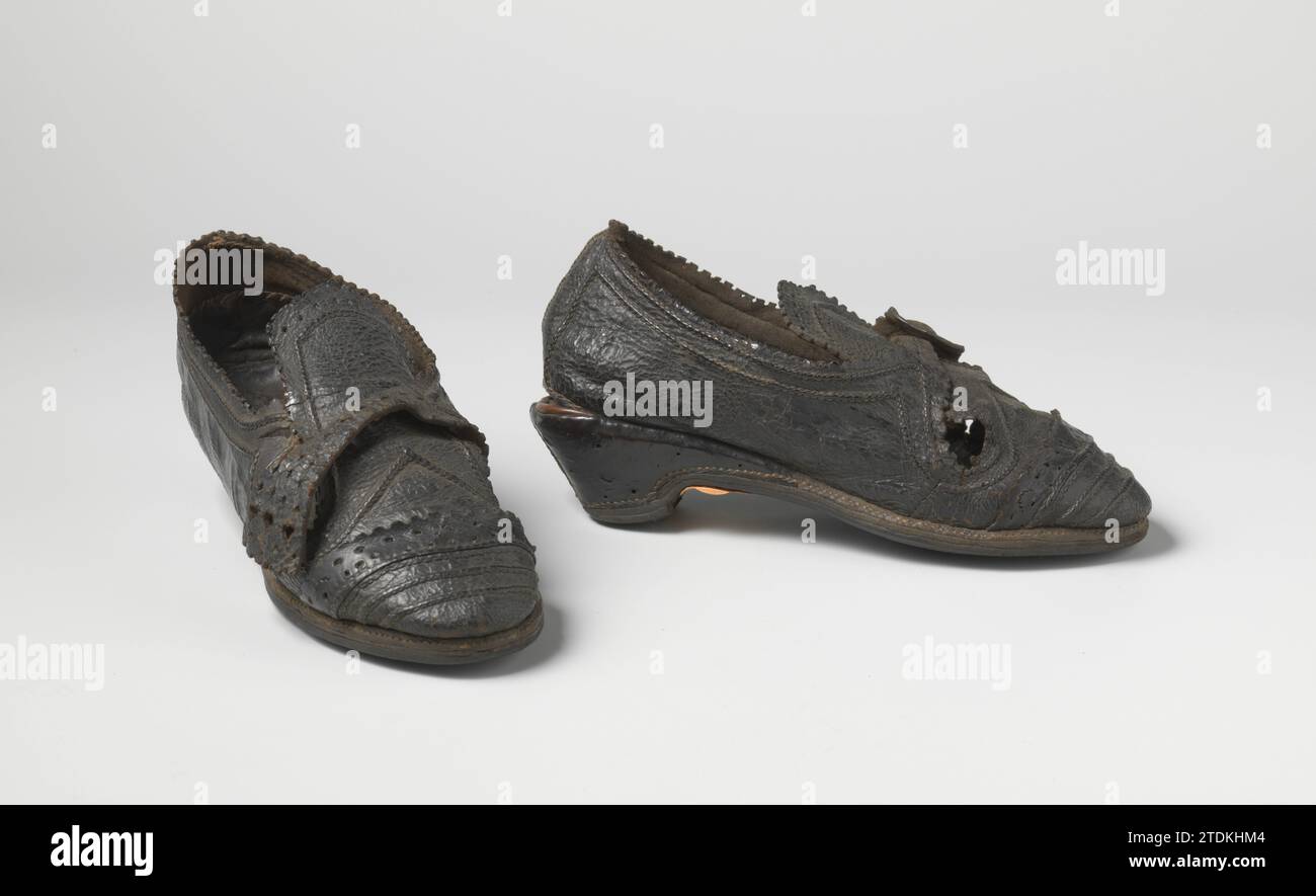 Women's shoe of beef leather with upright tongue, decorated with perforations and cartels, with low heel, anonymous, c. 1600 - c. 1650 Shoe of black leather. Left-right symmetrical. The cover is in a valve, on which a belt is closed. The block heel is partly loose, where a trim of red leather is applied. Decoration of two ramps, perforations and lectures. (related to BK-NM-8430). North Netherlands whole: Leather. perforating Shoe of black leather. Left-right symmetrical. The cover is in a valve, on which a belt is closed. The block heel is partly loose, where a trim of red leather is applied. Stock Photo