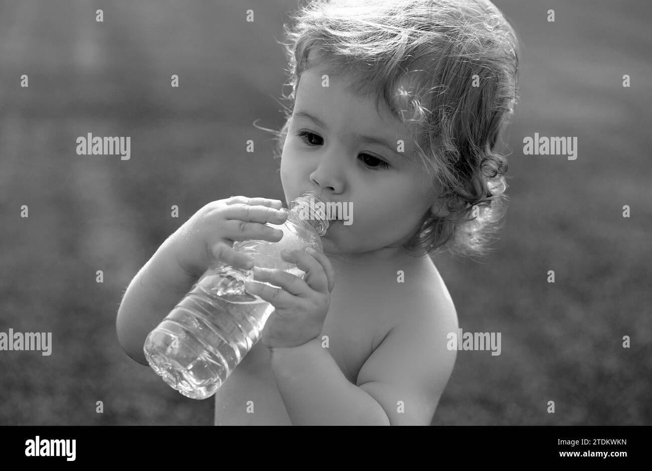 Child drinks water from a bottle while walking on grass field, baby health. Baby drinking water. Stock Photo