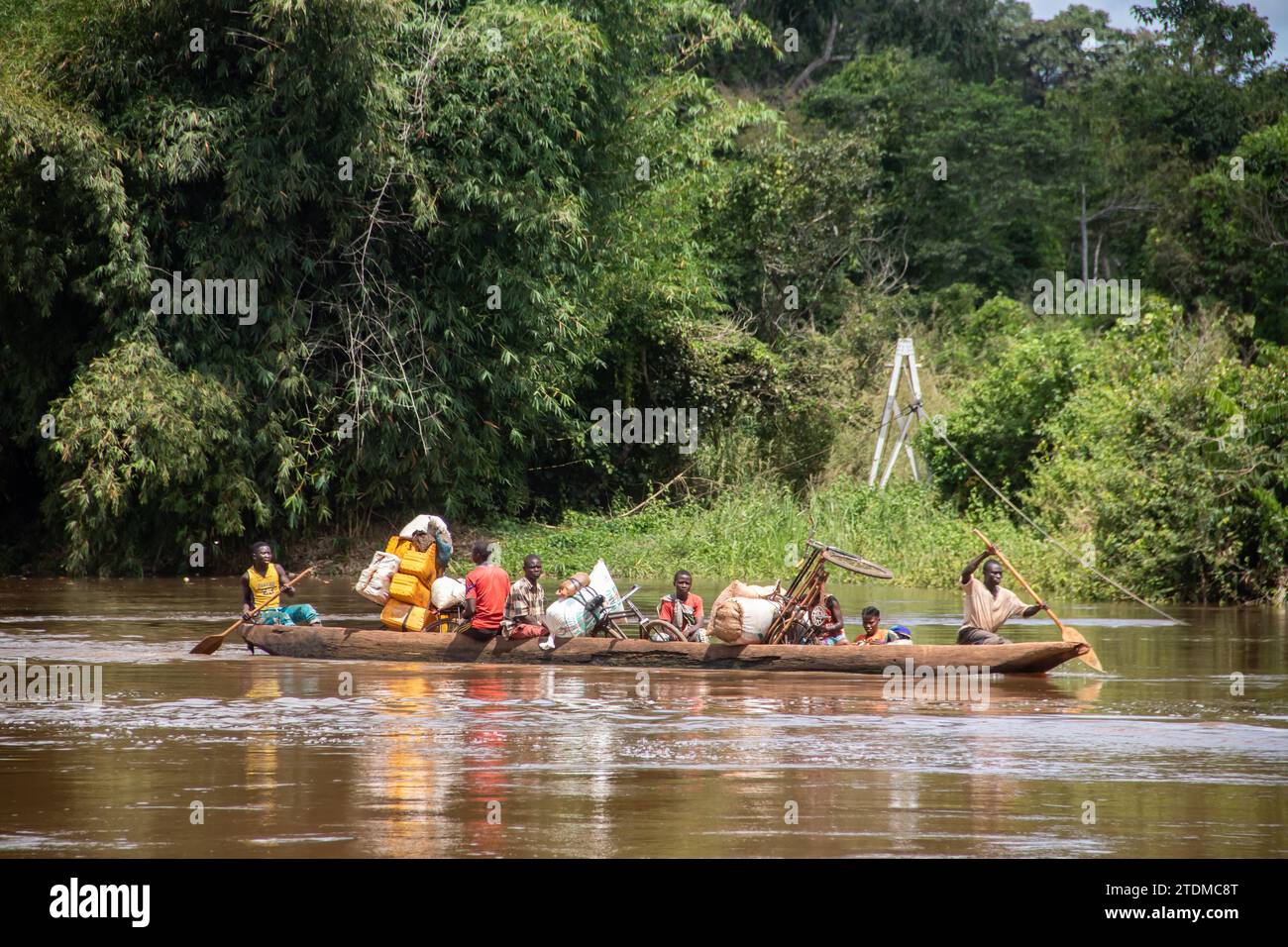 Transport of people across the Mbari river by locally made canoes and by ferry boat. Passengers colorfully dressed, transporting variety of goods Stock Photo