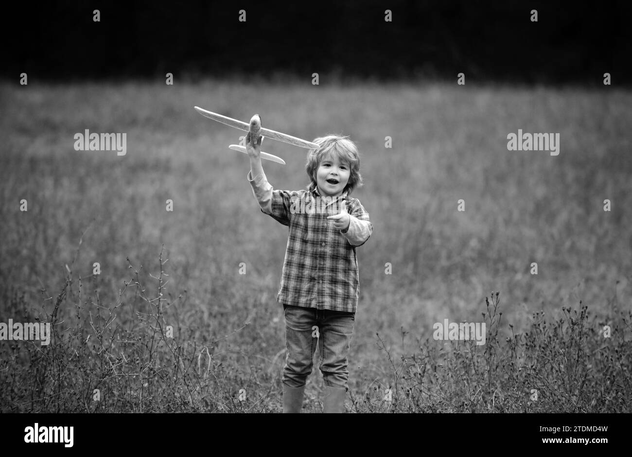Kid having fun with toy airplane in field. Little boy with wooden plane, boy wants to become pilot and astronaut. Happy child play with toy airplane Stock Photo