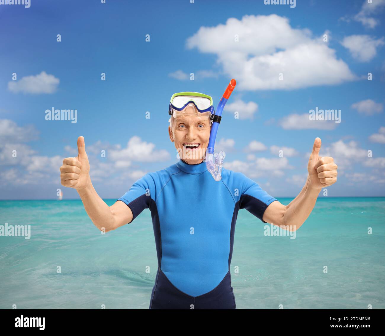 Cheerful senior man with snorkeling equipment wearing a wetsuit and making thumbs up sign in front of a sea Stock Photo